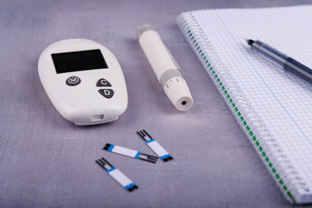 A glucometer with its sensors and needle placed next to a notebook for tracking results. Ideal for...