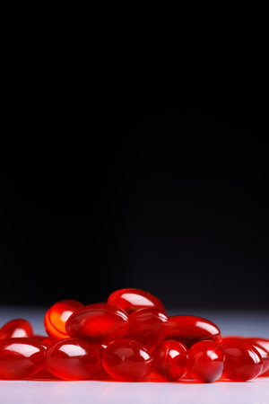 A detailed shot of a group of transparent red pills resting on a concrete surface, contrasted beautifully against a dark backgroundの写真素材