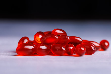 Close-up view of red transparent pills on a concrete table, with a striking black background that enhances their vivid color and textureの写真素材