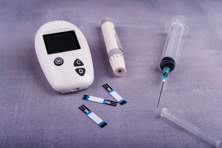 A glucometer, insulin syringe, and needle are displayed together, showing essential diabetes management tools on a clean surfaceの写真素材