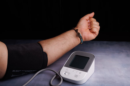 A person checks their blood pressure with a digital monitor on a concrete table, focusing on heart...