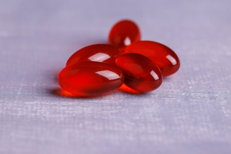 Close-up shot of several red transparent capsules on a concrete table, capturing their glossy surface and vivid hue in detailの写真素材