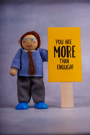 A wooden toy figure holds a yellow sign with a positive motivational phrase, symbolizing hope and encouragement, in a minimalist photo settingの写真素材