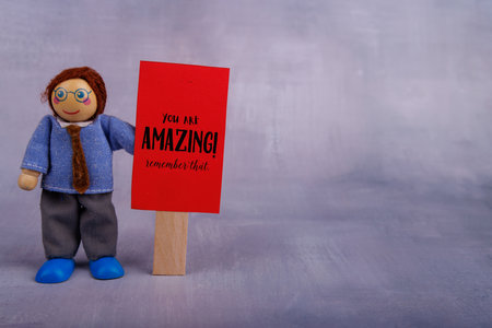 A smiling wooden toy man grasps a red motivational banner, radiating positivity and inspiring viewers to adopt a hopeful mindsetの写真素材