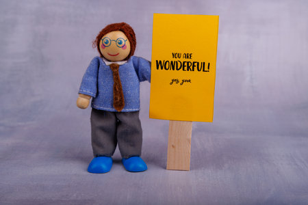 A joyful wooden toy figure displays a yellow banner with a positive quote, embodying inspiration and cheerful energy in a colorful environmentの写真素材
