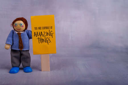 A wooden figure toy holds a yellow sign with a motivational message. The scene highlights encouragement and positivity with a simple, cheerful toneの写真素材