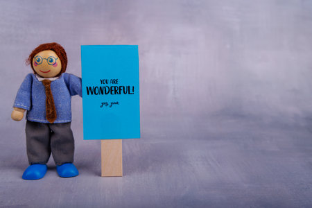This charming wooden toy holds a blue sign featuring a positive quote, embodying joy and motivation in a whimsical and fun wayの写真素材