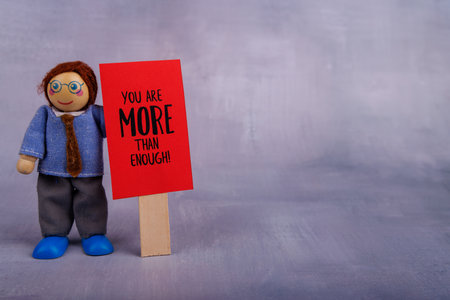A wooden toy man proudly displays a red sign featuring a motivational quote, spreading joy and positive energy to everyone who sees itの写真素材