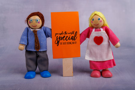 The wooden toy man and woman showcase a red banner featuring a positive phrase, inspiring viewers with their cheerful expressionsの写真素材