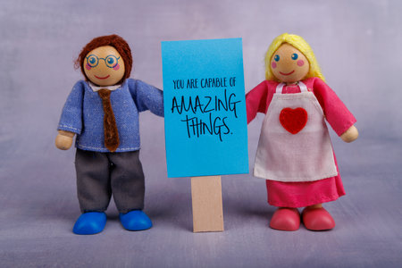 Two wooden toy figures, a man and a woman, are joyfully holding a blue banner with a motivational message, spreading positive vibes togetherの写真素材