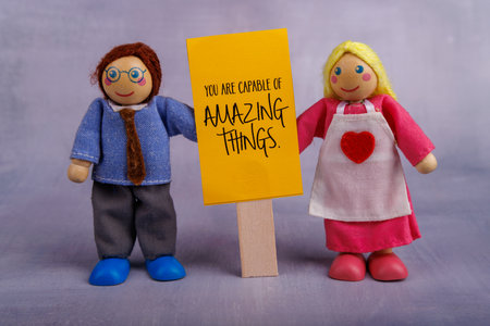 A wooden toy couple proudly displays a yellow sign with an inspiring message, promoting positivity and encouragement in a fun, creative sceneの写真素材
