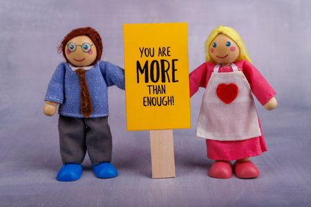A wooden toy couple holds a cheerful yellow banner featuring a motivational message, symbolizing...