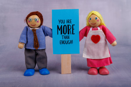 A charming wooden toy couple holds a blue banner displaying a positive quote, radiating joy and motivation in a vibrant, cheerful settingの写真素材