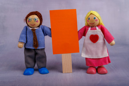 A man and woman toy figures made of wood hold a bright red and white banner, representing joy and positivity in a playful and colorful sceneの写真素材