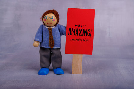 A whimsical wooden toy figure showcases a red motivational sign, promoting positivity and joy, perfect for brightening up any spaceの写真素材
