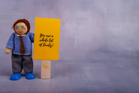 A charming wooden figure holds a yellow sign with an uplifting message. The image captures motivation and positive vibes with its simple, playful designの写真素材
