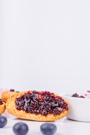 Toast covered with blueberry jam sits beside a jar on a white background, focusing on vibrant color and delicious textureの写真素材