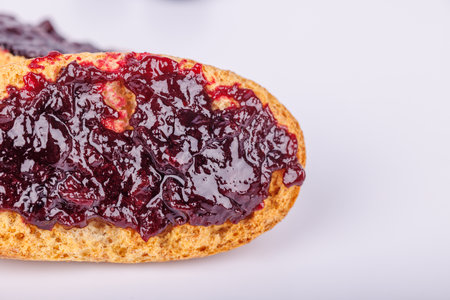 A close-up of toast spread with blueberry jam on a plain white background, showing rich colors and...