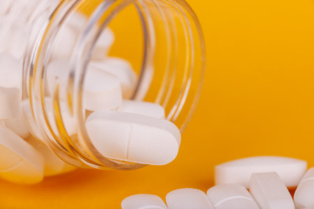 Transparent pill bottle with white pills on yellow, representing health and medical essentials