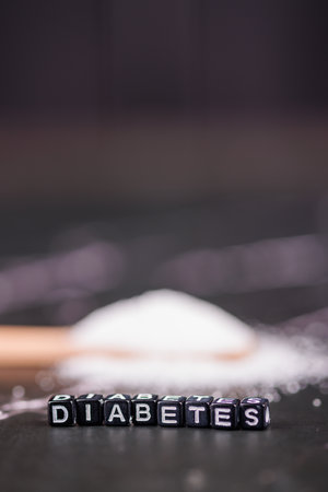 Spoonful of sugar and "diabetes" blocks on dark marble table, emphasizing the health risks and connection between sugar intake and diabetesの写真素材