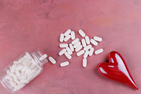 A Valentine's Day-inspired setup with red and white porcelain hearts and white pills on a red cement table, viewed from above, symbolizing heart diseaseの写真素材