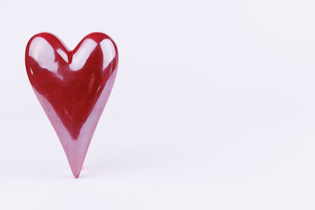 A striking red porcelain heart elegantly balanced on its tip against a clean white background, symbolizing love and romanceの写真素材