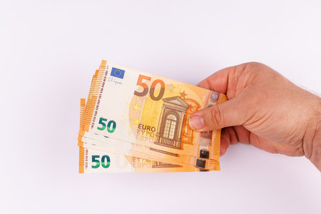 A compelling top-down view shows a hand holding several 50 euro banknotes on a clean white surface,...