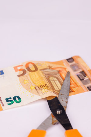A 50 euro banknote lies on a white surface, accompanied by scissors, symbolizing the act of cutting...