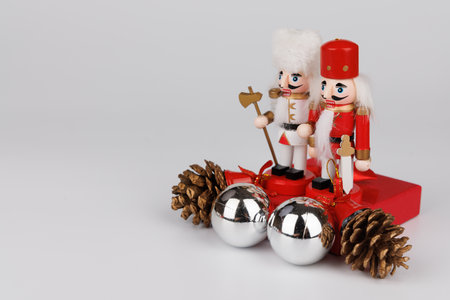 A charming pair of wooden nutcracker figurines rests on a red present, beautifully complemented by silver baubles and decorative pine conesの写真素材