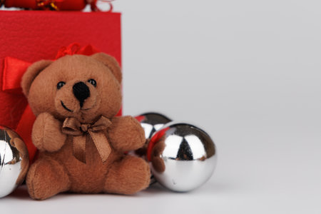 A festive wooden nutcracker stands next to a cuddly teddy bear, next to a red gift, adorned with silver ornaments and pine conesの写真素材