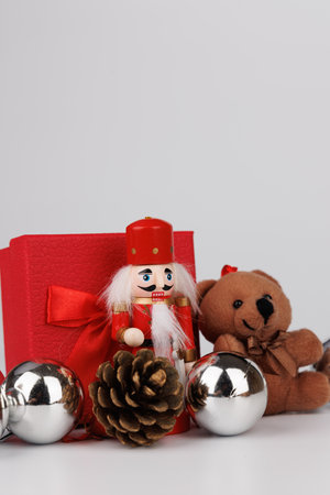 This festive nutcracker and plush bear are displayed next to a red gift, surrounded by silver ornaments and charming pine conesの写真素材