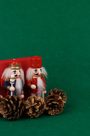 This joyful nutcracker and soft toy bear are positioned next to a red box, enhanced by silver accents and charming pine cones on greenの写真素材