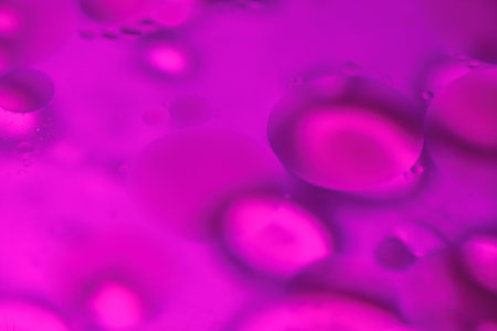 Floating oil droplets mix with water to form beautiful, organic abstract shapes, creating colorful...
