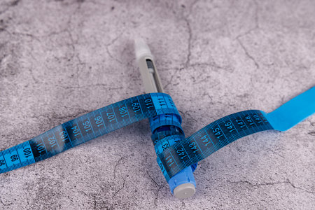 Injection pens and a blue measuring tape on a textured cement table background.