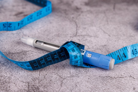 Glucose control pen with semaglutide, injection pens, and a blue measuring tape, displayed on a cement table surface.の写真素材