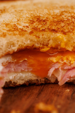 A vibrant half-eaten egg, ham, and cheese sandwich sits atop a vertical tower, beautifully arranged with red cherry tomatoes on a dark cutting boardの写真素材
