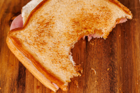 A vibrant half-eaten egg, ham, and cheese sandwich rests on a vertical tower, elegantly paired with...