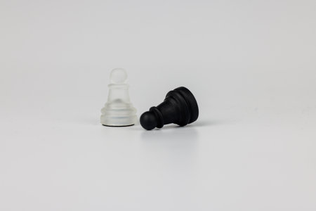 Transparent black and white glass pawns standing on a white background, reflecting strategy,...