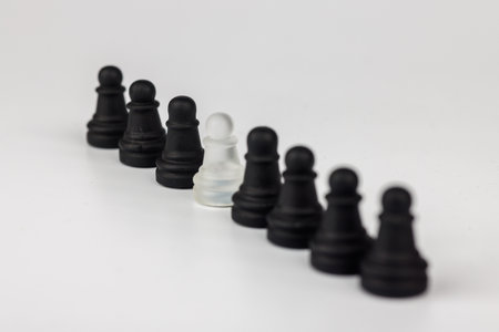 Strategic contrast: A lone white glass pawn among black chess pieces on a board, with a defeated...
