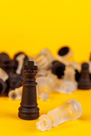 Strategic checkmate: black king dominates as white king surrenders, with fallen chess pieces in dramatic battle on yellow chessboardの写真素材