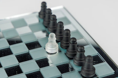White pawn confronting black pawns on a mirrored chessboard with a white background, symbolizing...