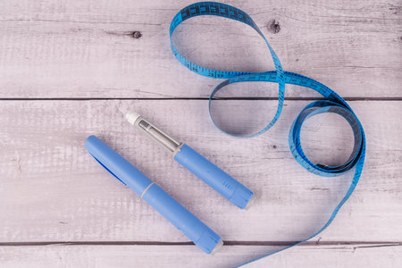 Top view of semaglutide injection pens and a measuring tape on a white wooden table, symbolizing weight loss and diabetes treatment in modern medicineの写真素材