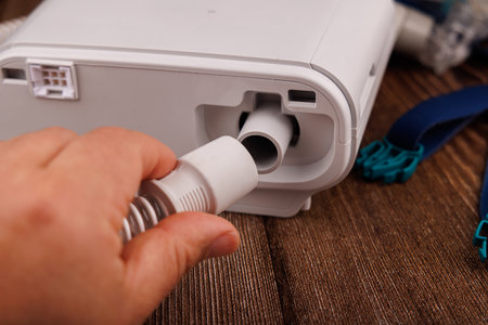 The image features a white CPAP machine with its display and mask, placed on a dark wooden table,...