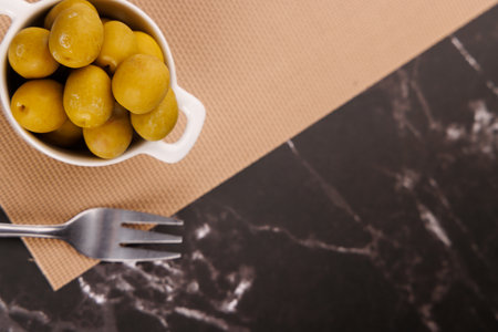 Flatlay shows hand picking olive with toothpick near oil bottle and olive bowl over a dark marble surfaceの写真素材