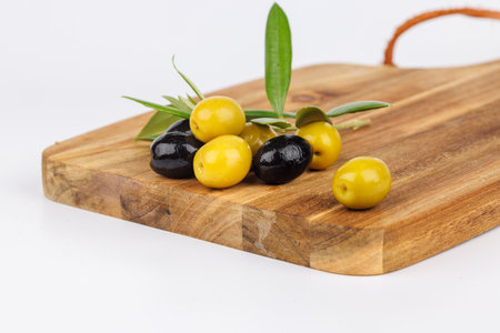 A simple and elegant arrangement of black and green olives with olive branches on a wooden board over whiteの写真素材