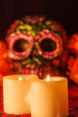 Painted skull and glowing candles rest among magnolias on a traditional cloth celebrating the Day of the Dead.の写真素材