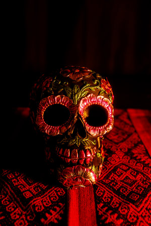 Painted black skull with floral decorations on a traditional cloth. A colorful altar honoring the...