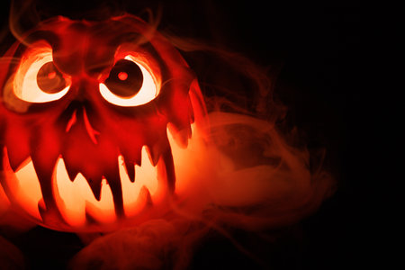 Halloween pumpkin carved with scary face glowing and smoke on black.の写真素材