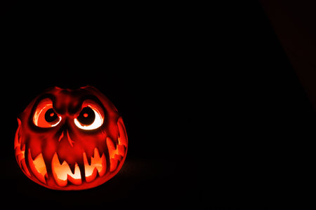 Spooky carved jack o lantern glowing with orange light in total darkness.の写真素材