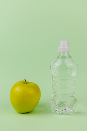 Self care composition with green apple and dual tone water bottles on light green backgroundの写真素材